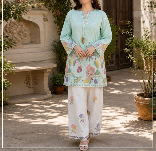 Mint green and white printed ethnic suit in an outdoor courtyard setting. The set features a long-sleeve kurta with colorful floral and leaf patterns, a matching embroidered neckline, and wide-leg palazzo pants.